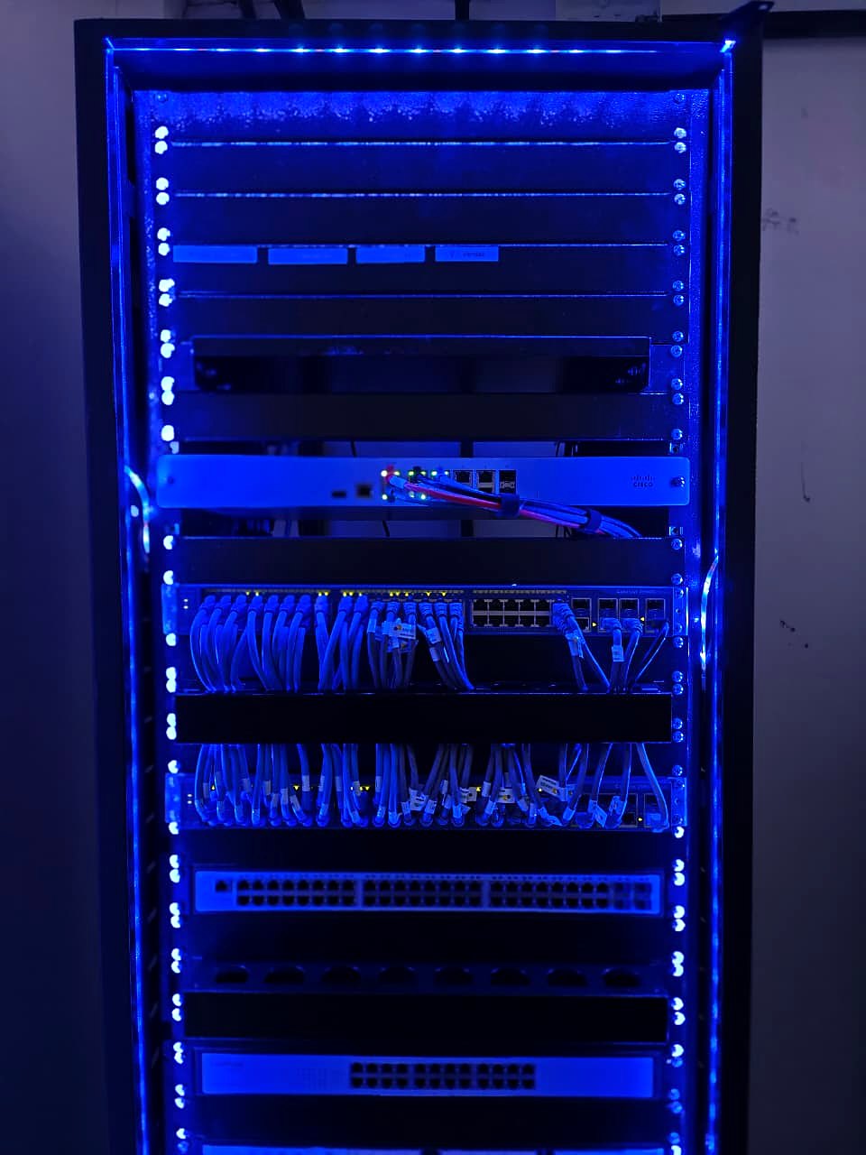 Detalhe do rack finalizado com iluminação LED azul, firewall, switches e patch panels