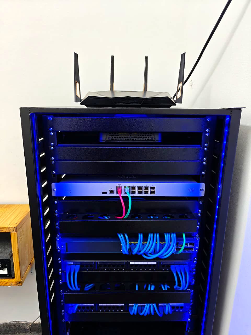 Detalhe do rack finalizado com iluminação LED azul, firewall, switch e patch panels com patch cords organizados