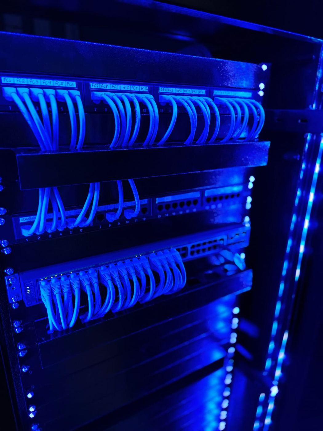 Detalhe dos patch panels e do switch com patch cords azuis organizados e iluminação LED azul lateral