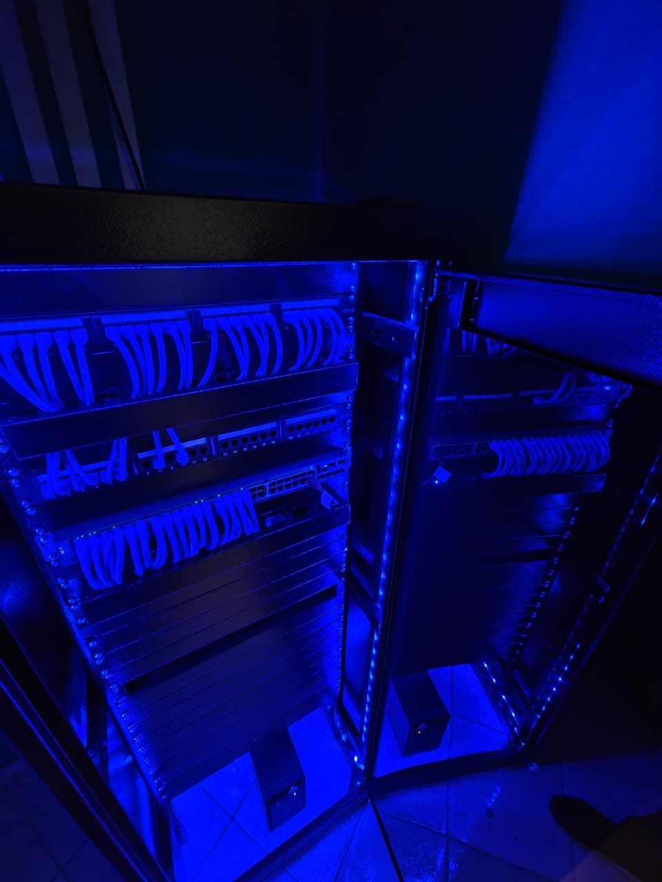 Interior do rack aberto com iluminação LED azul, destacando o cabeamento estruturado, o switch e os módulos de organização